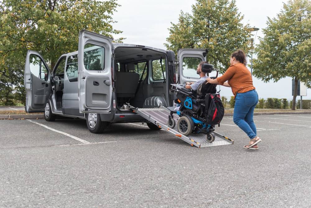 Assistant pushing a wheelchair rider up an accessible van ramp