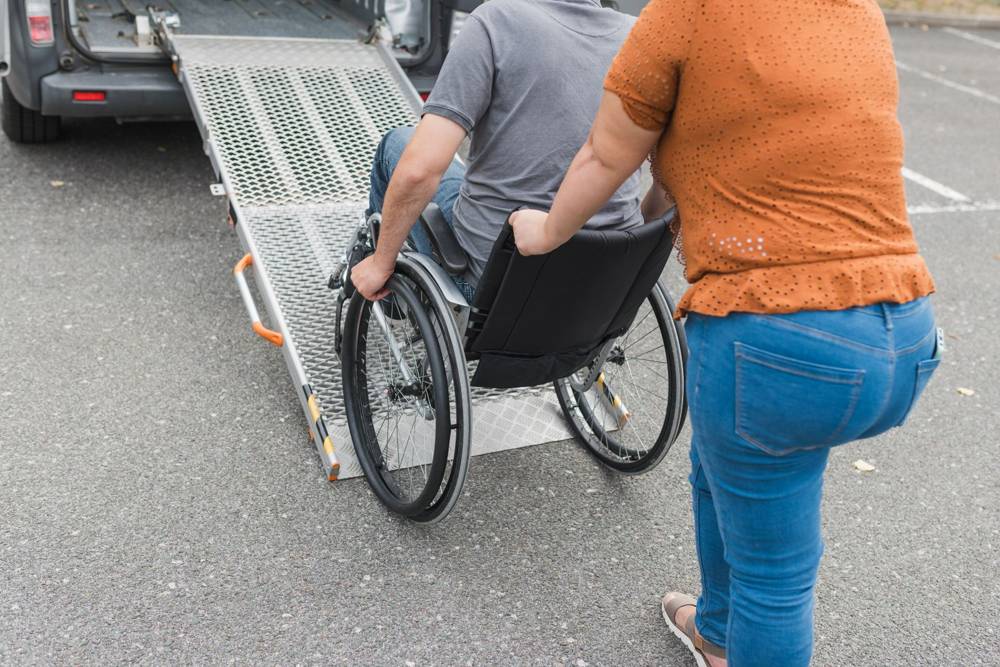 Assistant helping a wheelchair rider up a van ramp