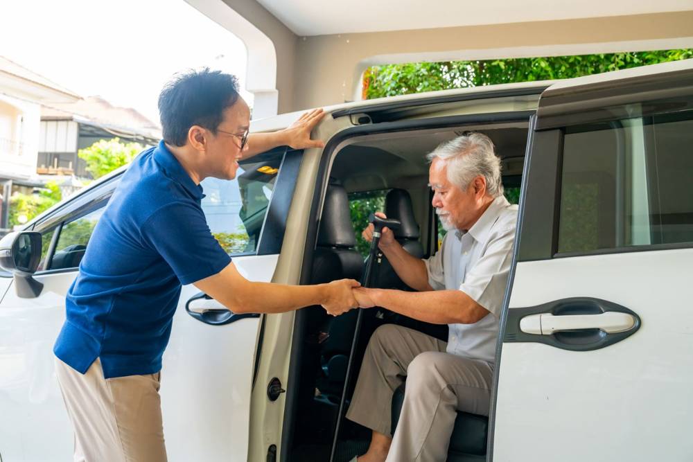 Caregiver helping a senior man into a car for a medical appointment